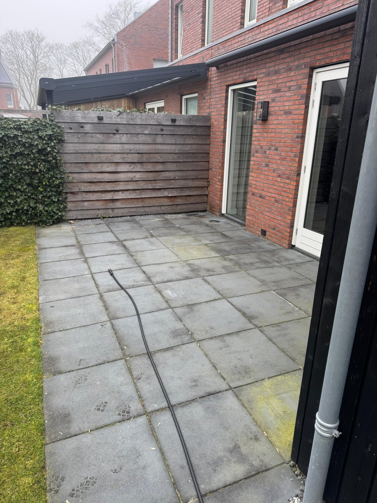 Tegelterras bij een rode gevel, dof en groenig uitgeslagen